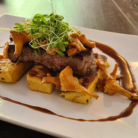 Auf einem weißen Teller angerichtetes Steak mit Beilagen aus Kartoffeln und Pfifferlingen.