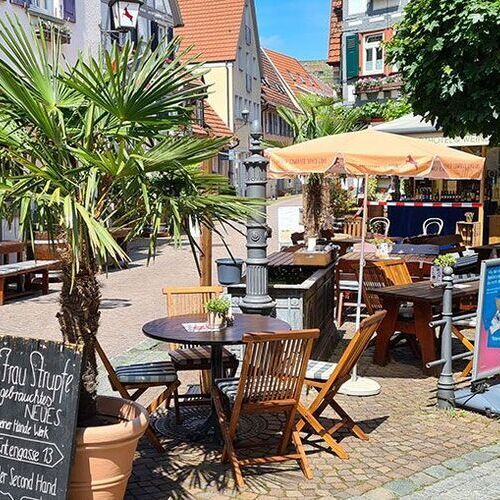 Eine belebte Straße mit Tischen und Stühlen vor einem Gebäude, das zum Entspannen und Verweilen einlädt.