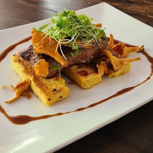 Auf einem weißen Teller angerichtetes Steak mit Beilagen aus Kartoffeln und Pfifferlingen.